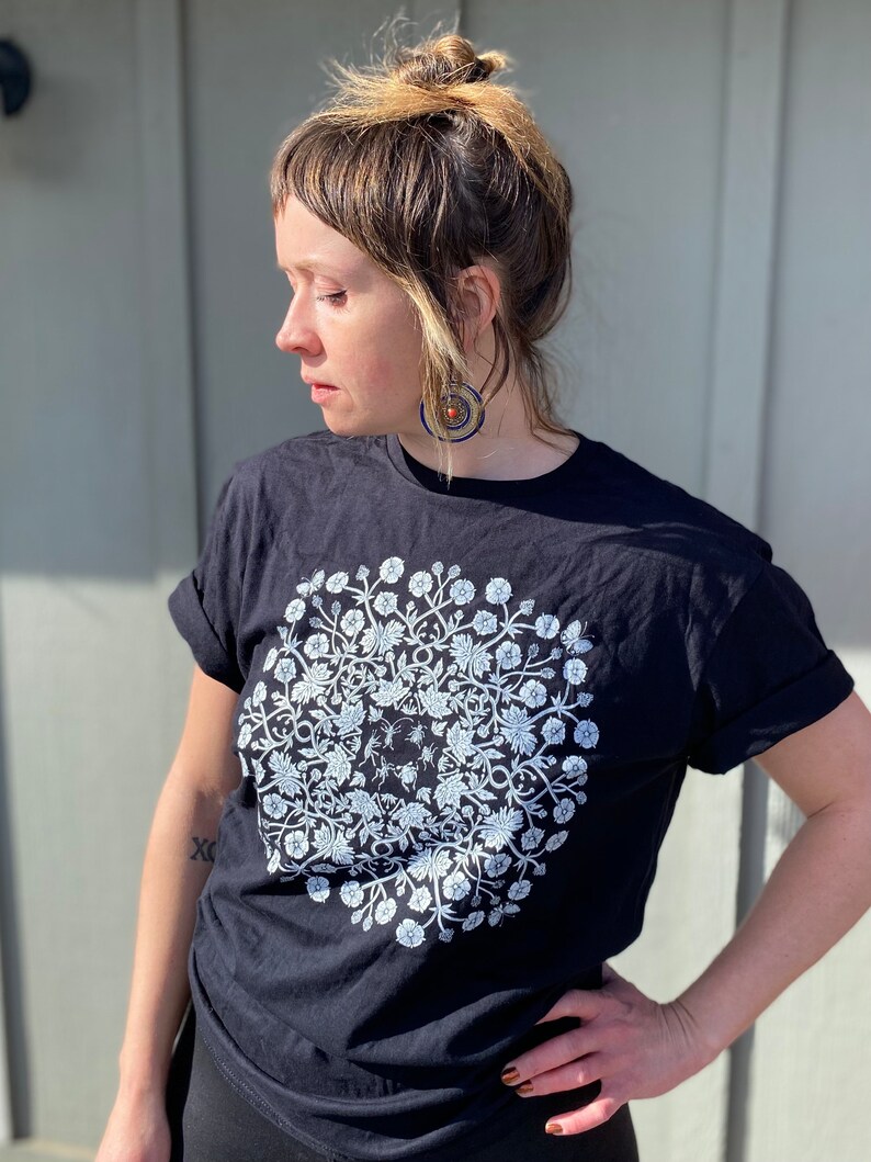 May include: A black t-shirt with a white floral mandala design. The mandala features a circular pattern of flowers and leaves.