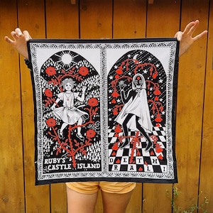 Peut inclure: Tapisserie noire avec deux illustrations. Le côté gauche représente une fille en robe blanche avec des fleurs rouges et le texte "Ruby's Castle Island". Le côté droit représente une figure en cape blanche avec des fleurs rouges et le texte "Death Realm".