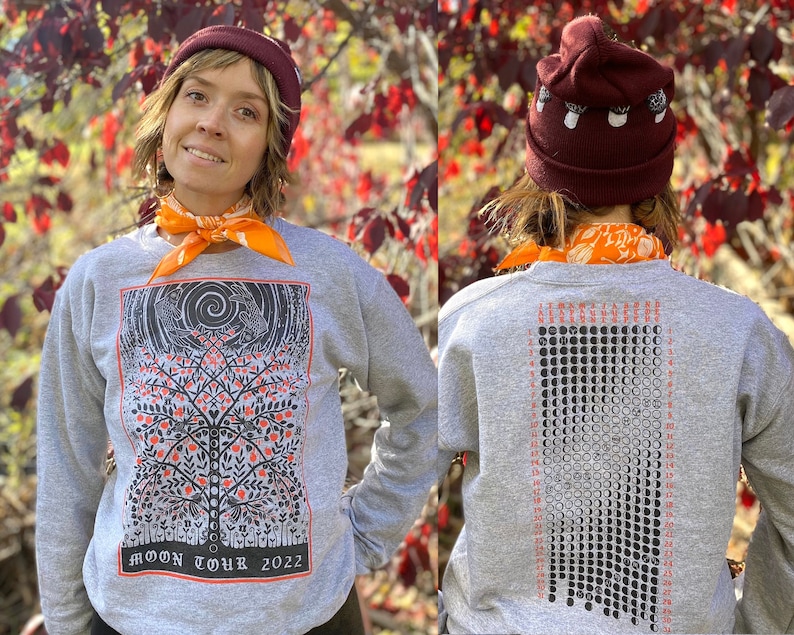 K&ouml;nnte beinhalten: Ein graues Sweatshirt mit einer schwarz-wei&szlig;en Illustration eines Baumes mit V&ouml;geln und einem Mond auf der Vorderseite. Die R&uuml;ckseite des Sweatshirts zeigt eine schwarz-wei&szlig;e Illustration eines Mondkalenders mit dem Text "MOON TOUR 2022".