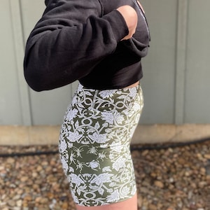 May include: A pair of green and white patterned bike shorts with a floral and insect design. The shorts are made of a stretchy fabric and have a high waist.