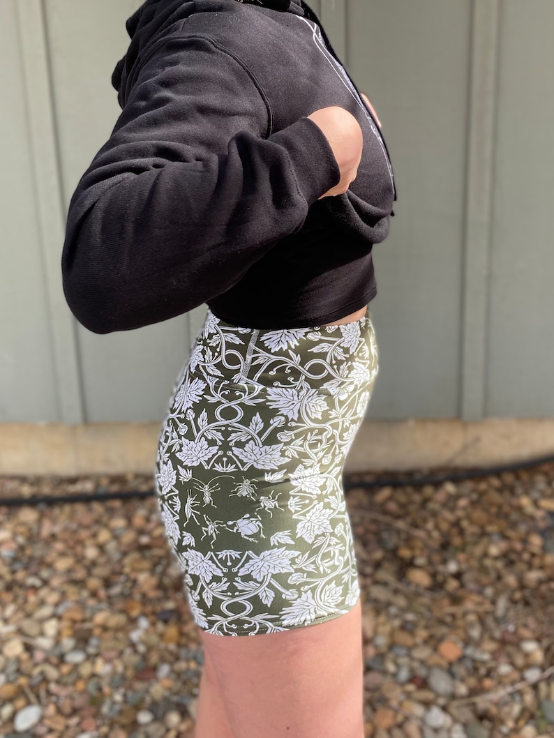 May include: A pair of green and white patterned bike shorts with a floral and insect design. The shorts are made of a stretchy fabric and have a high waist.