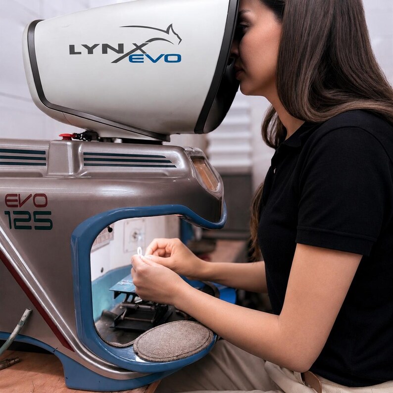 Pu&ograve; includere: Un microscopio stereo Lynx Evo 125 con un alloggiamento bianco e grigio metallizzato. Il dispositivo presenta una grande cappa di visione, un bordo blu attorno all'area di lavoro centrale e la scritta LYNX EVO ed EVO 125 sull'esterno.