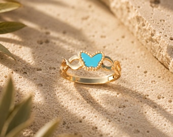 May include: A gold-toned ring featuring a central butterfly motif with bright turquoise enamel inlay. The band has an open, swirling design on both sides of the butterfly, creating a delicate and symmetrical appearance for this piece of jewelry.