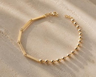Può includere: Un bracciale color oro caratterizzato da un design a doppia catena. Una metà del bracciale è composta da maglie rettangolari lisce, mentre l'altra metà è formata da piccole perline sferiche rotonde. Il gioiello include una chiusura a molla.