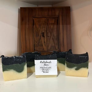 Peut inclure: Quatre savons faits à la main avec des tourbillons noirs et verts. Le savon est étiqueté "Patchouli Bar with Activated Charcoal & Spirulina Powder".