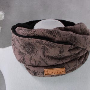 Könnte beinhalten: Ein taupefarbener Loop-Schal mit schwarzem Innenfutter und floralem Muster. Der Schal ist um eine weiße Schaufensterpuppe gewickelt. Ein kleines braunes Lederetikett ist am Schal befestigt.