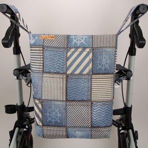 Könnte beinhalten: Eine rechteckige Stofftasche mit einem blau-weißen Patchwork-Muster, das nautische Motive wie Anker und Steuerräder zeigt. Die Tasche hat zwei Trageriemen und ist an einem schwarz-silbernen Gehwagen aus Metall mit Rädern befestigt.