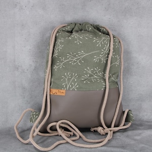 Könnte beinhalten: Ein grüner Rucksack mit Kordelzug, einem weißen Blumenmuster und einem braunen Lederboden. Der Rucksack hat ein braunes Lederetikett mit dem Text "Hu Hu" darauf.