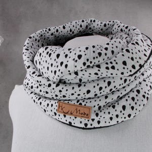 Könnte beinhalten: Ein weiß-schwarzer Loop-Schal, der auf einer Schaufensterpuppe präsentiert wird. Der Schal hat einen schwarzen Rand und ein kleines braunes Etikett mit der Aufschrift "HK Mode". Der Schal ist aus einem weichen, leichten Material gefertigt.