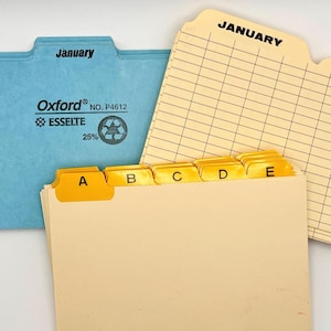 May include: A blue Oxford file folder labeled January, a cream-colored monthly calendar folder with January and February headers, and a cream-colored file folder with yellow A, B, C, D, and E index tabs. The blue folder features the text Oxford NO. P4612 ESSELTE.