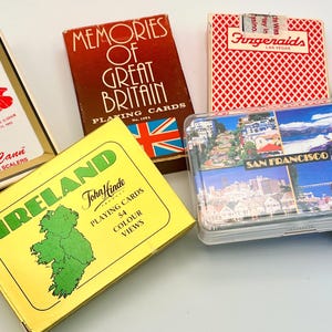 May include: A collection of six decks of playing cards in various boxes, including a yellow Ireland box, a red Memories of Great Britain box, a Las Vegas Ameri-Cann box, a red patterned Fitzgeralds box, a San Francisco box, and a Notre Dame box.