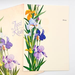 May include: Two cream-colored stationery cards featuring a vertical floral illustration of yellow, light blue, dark blue, and purple iris flowers with green leaves. The left card displays the text Just a Note, and the right card displays the word Stamp.