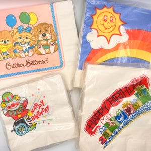 May include: Four packs of paper napkins featuring various illustrations. One pack shows three animals with balloons and the text Critter Sitters. Another displays a sun and rainbow. A third features a clown with Happy Birthday text. The last shows a train.