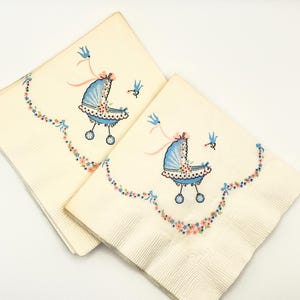 May include: Two off-white paper napkins with a baby carriage design. The carriage is light blue with pink accents and floral details. A garland of flowers and bows surrounds the carriage, with a blue bird flying nearby.