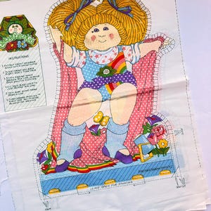 May include: A fabric panel featuring a Cabbage Patch Kids doll design. The doll has blonde hair, blue bows, and is wearing a colorful outfit with a rainbow and star accents. Instructions for sewing are printed on the panel.