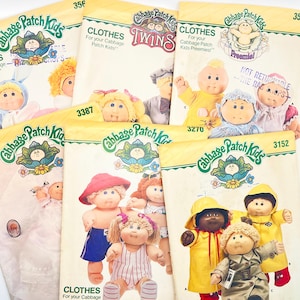 May include: A collection of vintage Cabbage Patch Kids clothing patterns. The covers feature illustrations of the dolls in various outfits, including a bunny costume, raincoats, and swimwear. The patterns are labeled with the Cabbage Patch Kids logo and the word "CLOTHES".