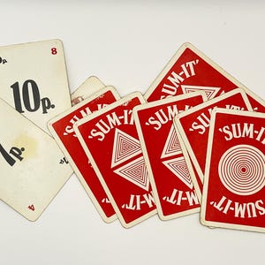 May include: A collection of vintage playing cards. Some cards are white with black numbers and text, while others are red with white text and geometric designs. The text on the red cards reads "SUM-IT".