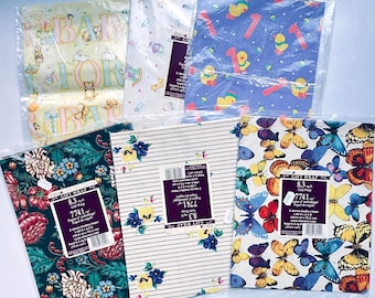May include: Assortment of gift wrap sheets in plastic packaging. Designs include baby-themed patterns, a blue sheet with ducks and the number 1, floral patterns, and a butterfly print. Each sheet is 8.3 sq ft.