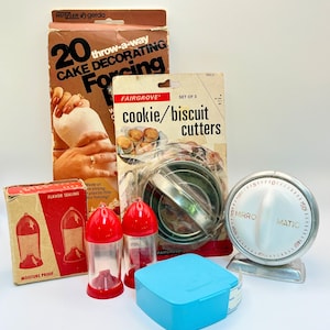May include: A collection of vintage kitchen tools, including a cake decorating kit, cookie cutters, spice shakers, a timer, and a blue container. The items are in their original packaging, with a retro aesthetic.