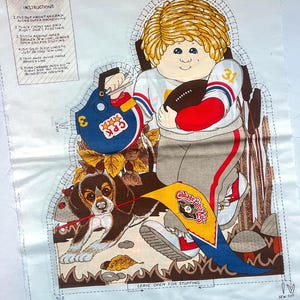 May include: A fabric panel featuring a vintage Cabbage Patch Kids design. The illustration depicts a boy in a football uniform with a football, a helmet, and a beagle. Instructions are printed on the left side.