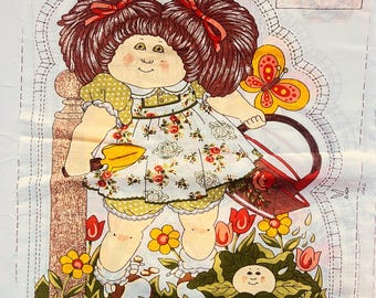 May include: A vintage Cabbage Patch Kids fabric panel with a doll design. The doll has brown hair with red bows, a floral dress, and is surrounded by flowers and a butterfly. Instructions are printed on the fabric.