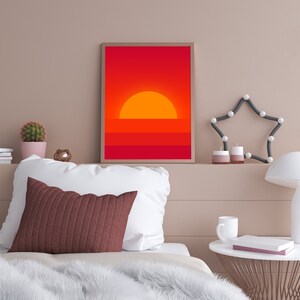 May include: A framed print of a minimalist sunset with a red and orange color scheme. The print is hanging on a wall above a bed with white bedding and a brown throw blanket.
