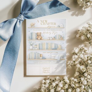 May include: Baby shower invitation with a blue ribbon. The invitation features a bookshelf design with a teddy bear, books, and the text "A New Chapter Begins" and "Kimberly Taylor". The date and time are also included.