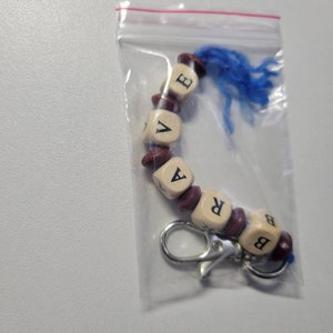 May include: A keychain with a blue tassel and wooden beads spelling out the word "BRAVE".