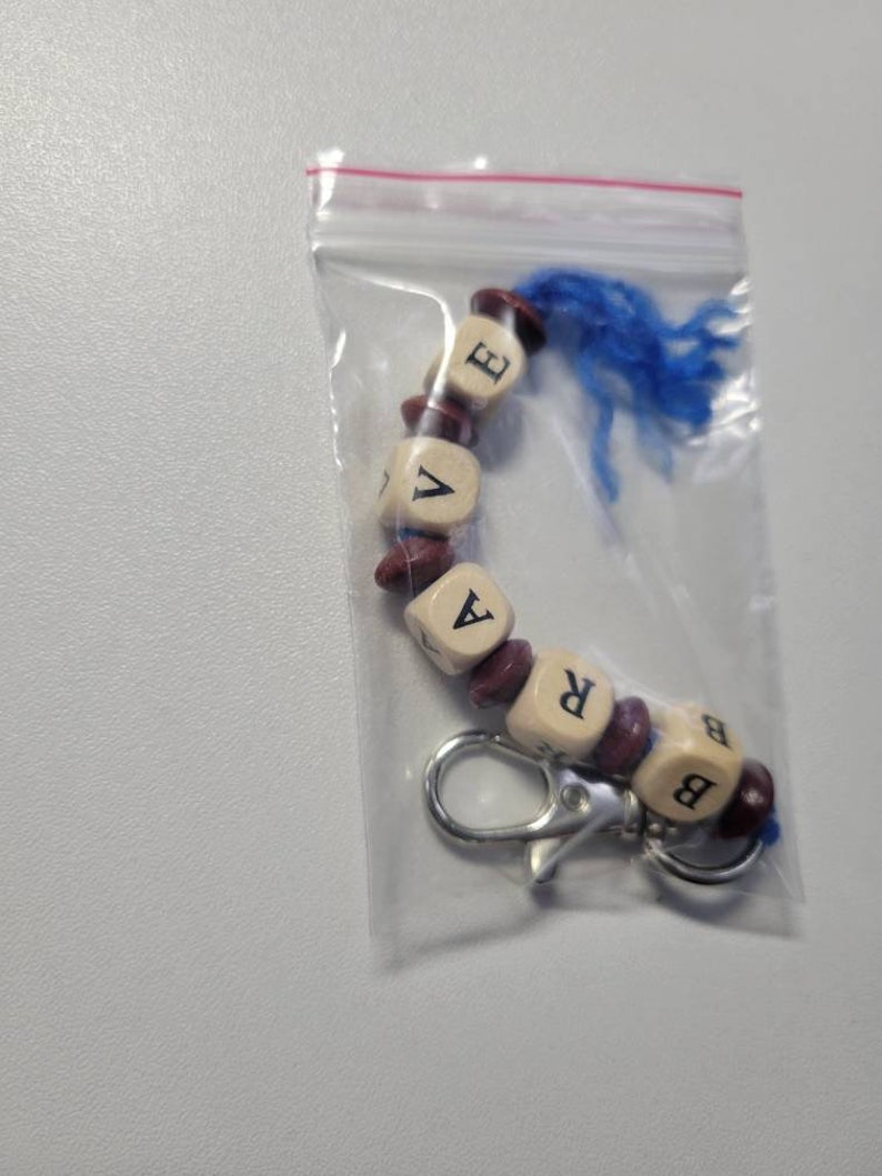 May include: A keychain with a blue tassel and wooden beads spelling out the word "BRAVE".