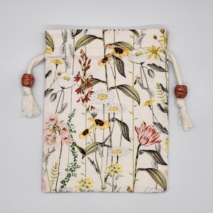May include: A white drawstring bag with a floral print featuring red, yellow, and pink flowers. The bag has a white drawstring with brown wooden beads.