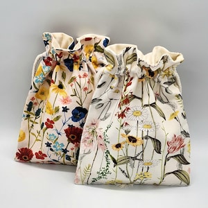 May include: Two drawstring bags with floral patterns. The bag on the left has a red, yellow, blue, and white floral pattern. The bag on the right has a white, yellow, and green floral pattern.