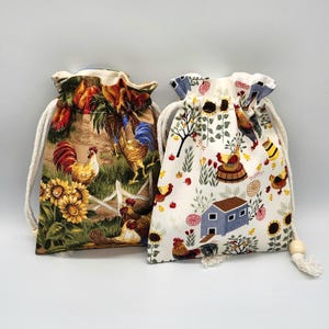 May include: Two drawstring bags with farm animal patterns. One bag features roosters, sunflowers, and a white fence on a beige background. The other bag has a white background with chickens, a blue house, and sunflowers.