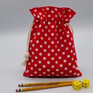 May include: Red fabric drawstring bag with white polka dots, two yellow dice, and two yellow pencils with the text "American Pencil - U.S.A. Gold" printed on them.