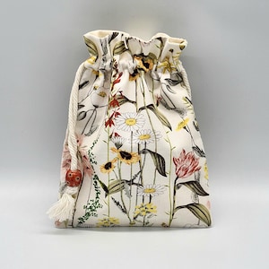 May include: A white drawstring bag with a floral print featuring various flowers, including daisies, sunflowers, and red tulips. The bag has a white drawstring with a red bead.