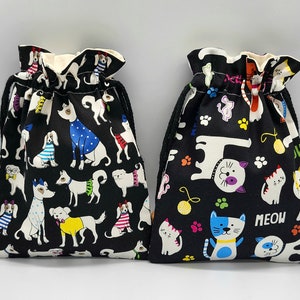 May include: Two black drawstring bags with different animal prints. One bag features a black and white dog print with colorful accents. The other bag features a black and white cat print with colorful accents. The cat bag has the word "MEOW" printed on it.