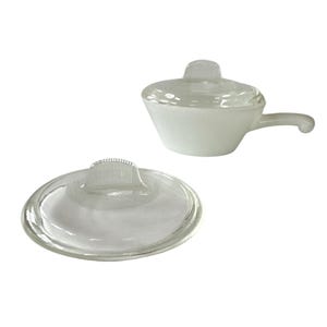 May include: A small, white, glass saucepan with a handle and a clear glass lid. The lid has a small, rectangular handle. The saucepan is sitting next to the lid, which is also clear glass.