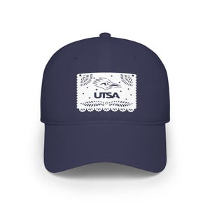 Può includere: Cappellino da baseball blu navy con una toppa rettangolare bianca con la scritta "UTSA" e un logo di roadrunner. La toppa ha un bordo decorativo ritagliato. Il cappellino ha una visiera curva e una corona strutturata.