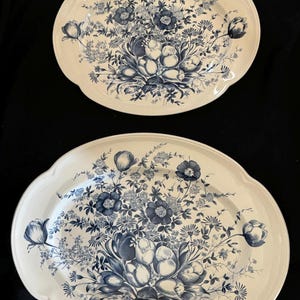 May include: Two oval serving platters with a cream-colored background and a blue floral design. The floral pattern includes various flowers and foliage. The platters have a scalloped edge.