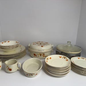 May include: A set of vintage Autumn Leaf dinnerware, including plates, bowls, a casserole dish, and a sugar bowl. The dishes feature a white background with a pattern of orange, brown, and yellow leaves.