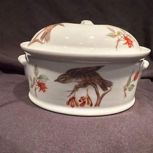 May include: White ceramic oval baking dish with a lid. The dish has a brown bird perched on a branch with red berries and green leaves. The lid has a brown bird and red flowers.