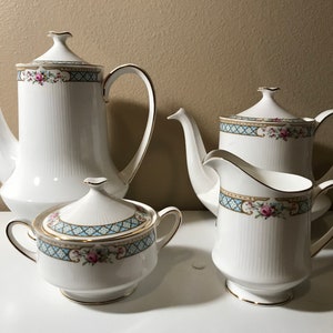 May include: A white porcelain tea set with a blue and gold floral pattern. The set includes a teapot, creamer, sugar bowl, and lid.
