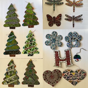 May include: A collection of mosaic ornaments featuring six green Christmas trees, three dragonflies, one butterfly, a flower, a paw print, the letter H, a small circular snowman, and two hearts, all crafted from various colored glass pieces.