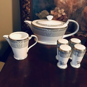 May include: A set of white porcelain teaware with a silver trim and a gray and white floral pattern. The set includes a teapot, creamer, and four salt and pepper shakers.