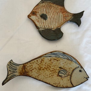 May include: Two ceramic fish sculptures. One is a brown and white angelfish with blue accents. The other is a brown and white fish with blue accents.