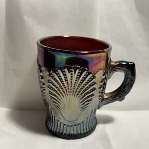 May include: A vintage iridescent purple glass mug with a scalloped shell design. The mug has a handle and is perfect for serving beverages.