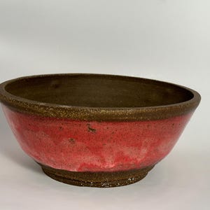 May include: A large, red and brown ceramic bowl with a speckled glaze. The bowl is round and has a wide rim.