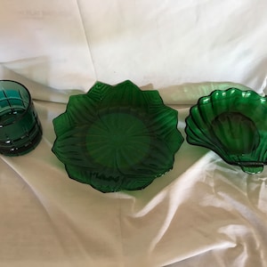 May include: Three green glass dishes, one is a round plate with a scalloped edge, one is a shallow bowl with a scalloped edge, and one is a tall glass with a geometric pattern.
