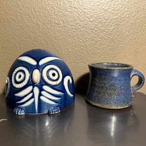 May include: A blue ceramic owl figurine with white details and a blue ceramic mug with a speckled glaze.