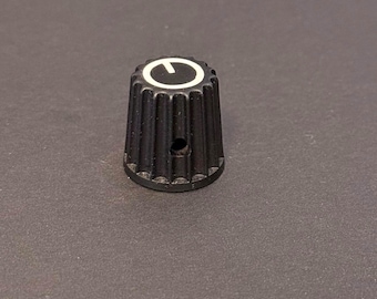 Könnte beinhalten: Ein schwarzer Drehknopf mit weißer Markierung. Der Knopf hat eine geriffelte, konische Form und ein kleines Loch. Der Knopf dient wahrscheinlich zum Einstellen von Einstellungen an elektronischen Geräten.