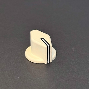 May include: Cream-colored control knob with a geometric design. The knob features a rounded base and a slanted top with a black and white stripe. The knob is likely for an electronic device or musical instrument.